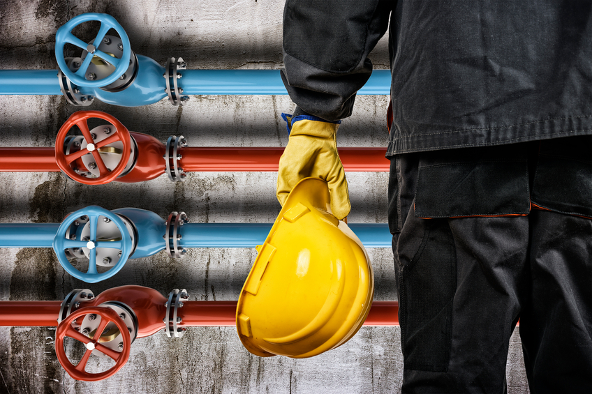 worker with protective helmet in front of industrial refinery oil pipes with valves